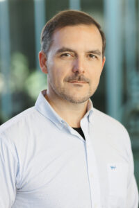 Photo of Brian Harris wearing a white shirt standing in front of a blurred background