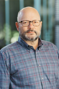 Photo of Kai Gray wearing a blue striped shirt standing in front of a blurred background